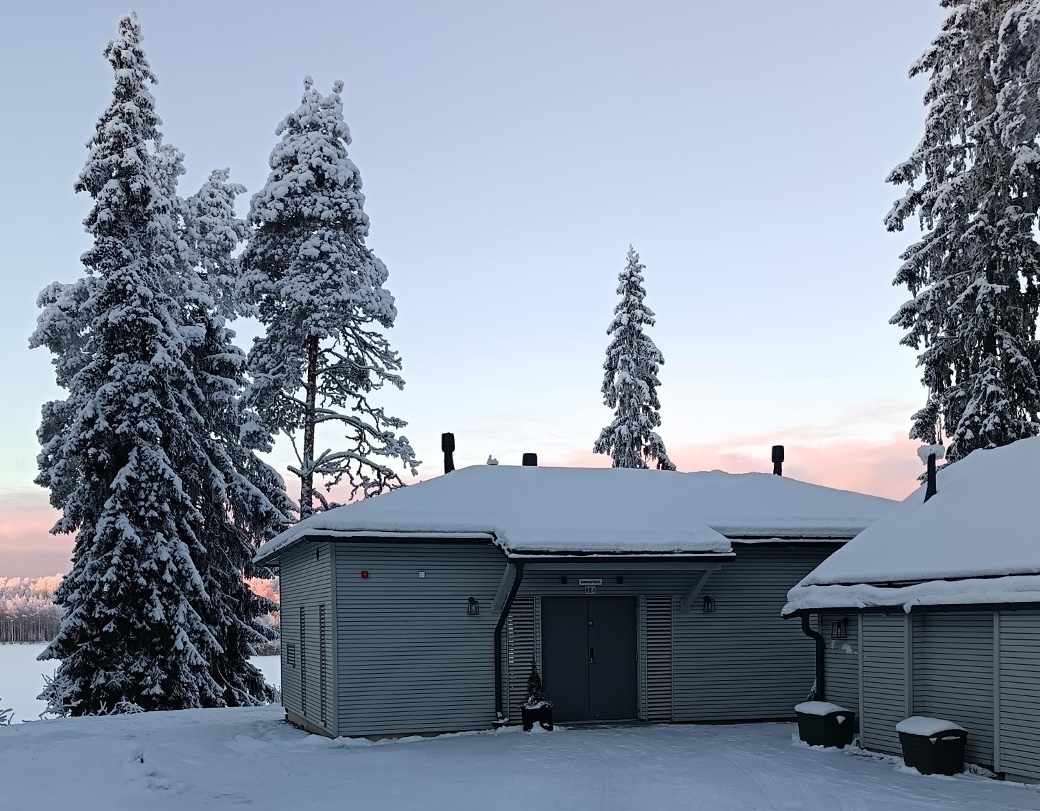 Kirkkotupa, lumisten puiden vierellä, taustalla jokimaisema