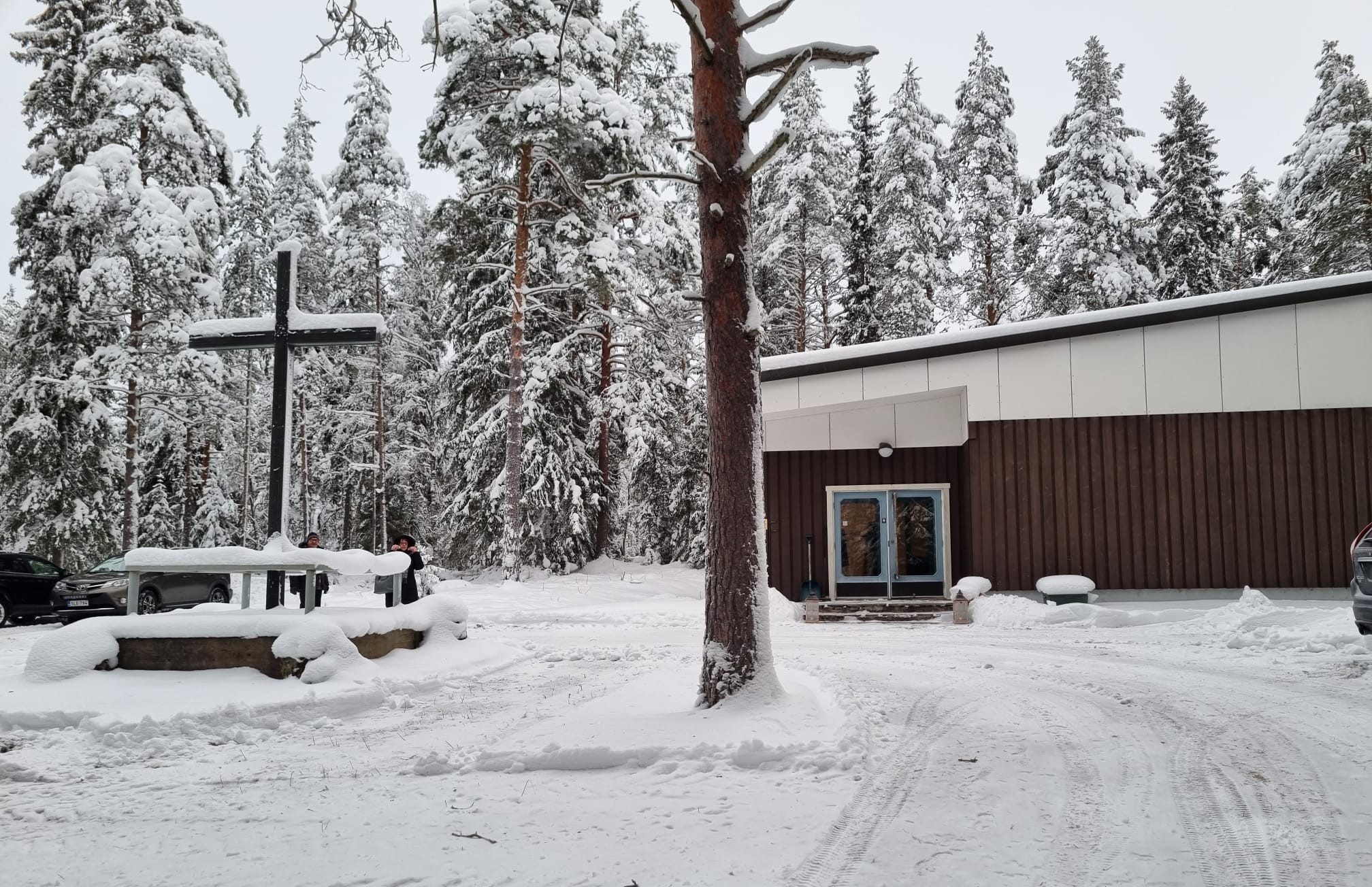 Kylmälänkylän kappeli, luminen maisema ja männyt ympärillä, iso risti pihalla